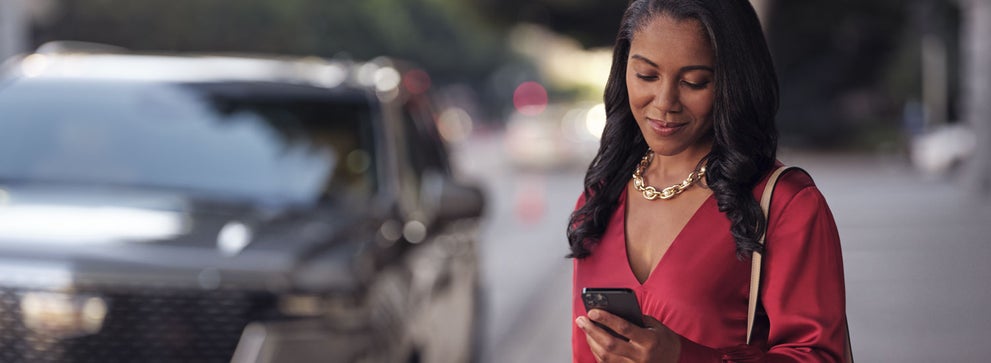 lady checking her mobile with a Cadillac vehicle background | D'ELLA Cadillac in QUEENSBURY NY